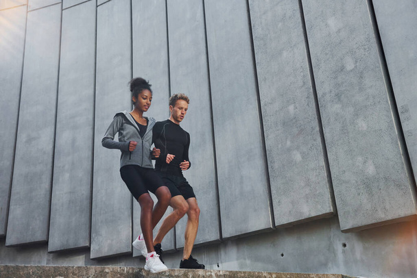 Near big wall. European man and african american woman in sportive clothes have workout together. - Fotografie, Obrázek