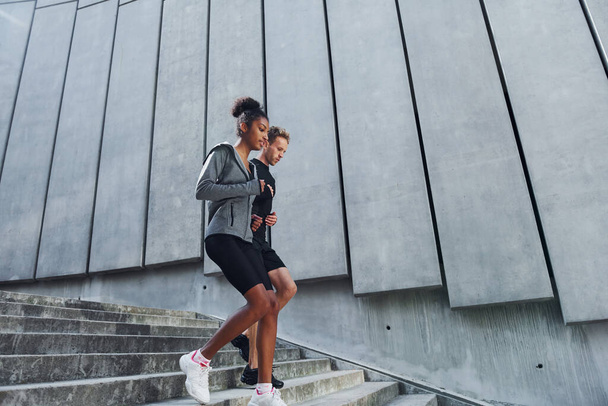Near big wall. European man and african american woman in sportive clothes have workout together. - Φωτογραφία, εικόνα