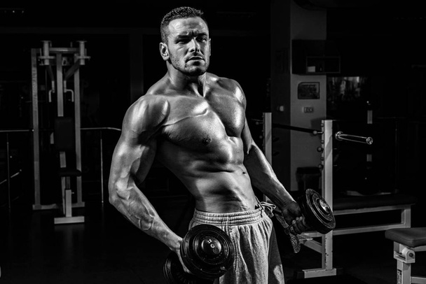 Athletic man bodybuilder doing exercises with dumbbell. Fitness muscular body. Gym training. - Valokuva, kuva