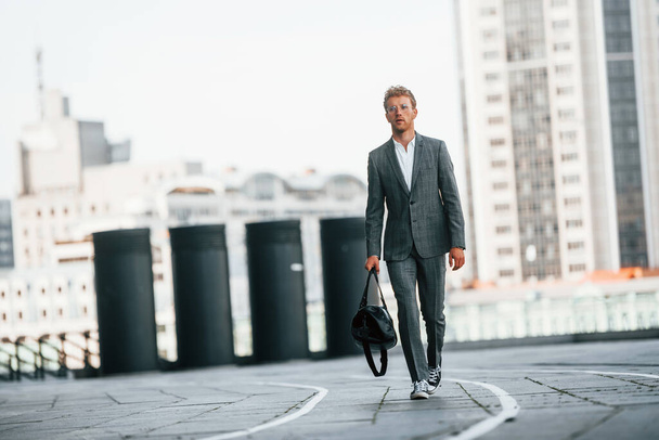 Walks on the road. Young businessman in grey formal wear is outdoors in the city. - Fotoğraf, Görsel