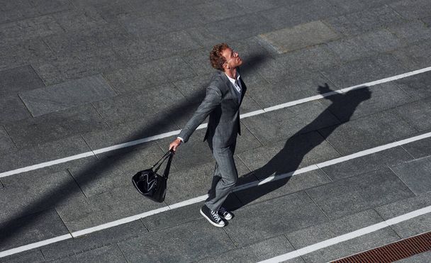 Dancing, celebrating success. Young businessman in grey formal wear is outdoors in the city. - Foto, Imagen