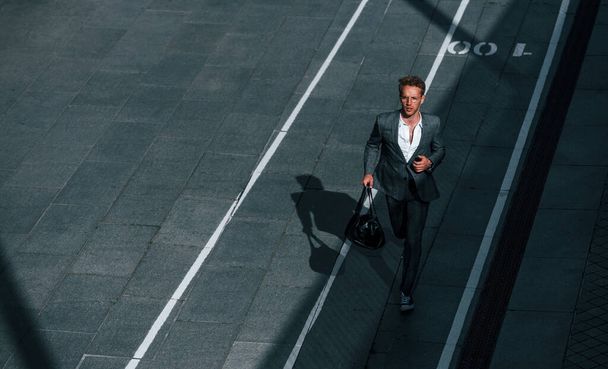 View from the top. Young businessman in grey formal wear is outdoors in the city. - 写真・画像