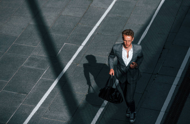 View from the top. Young businessman in grey formal wear is outdoors in the city. - 写真・画像