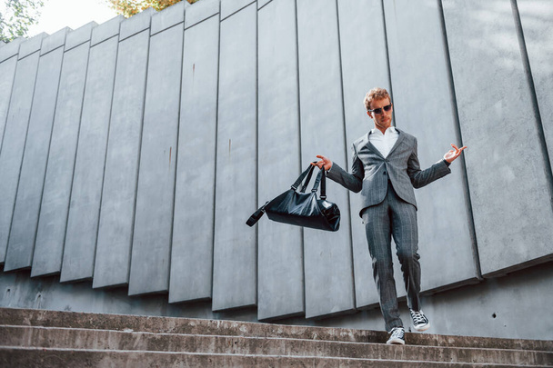 Going down by the stairs. Young businessman in grey formal wear is outdoors in the city. - Photo, Image