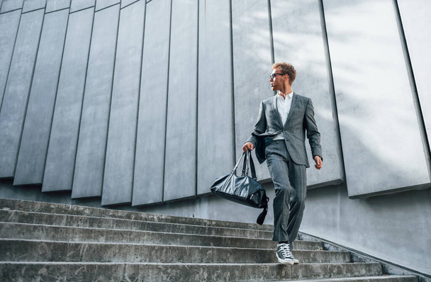 Going down by the stairs. Young businessman in grey formal wear is outdoors in the city. - Fotografie, Obrázek