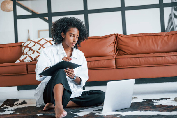 With laptop. Young african american woman with curly hair indoors at home. - Foto, imagen