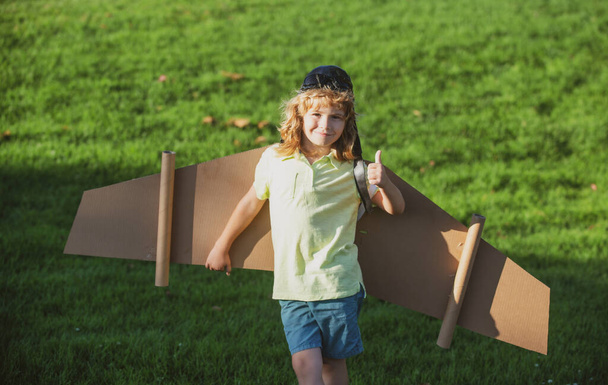 Kids fly. Funny child boy with thumbs up smile wear pilot hat and goggles flying with toy cardboard airplane wings, Start up freedom concept, carefree kid. - Φωτογραφία, εικόνα
