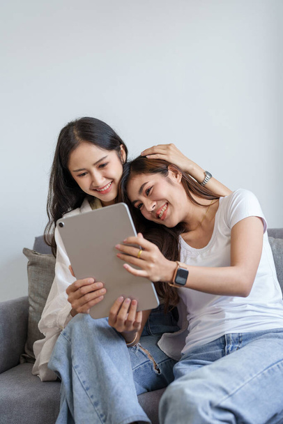Igbtq, Igbt concept, ομοφυλοφιλία, πορτραίτο δύο Ασιάτισσων γυναικών που απολαμβάνουν μαζί και δείχνουν αγάπη η μία για την άλλη ενώ χρησιμοποιούν tablet - Φωτογραφία, εικόνα