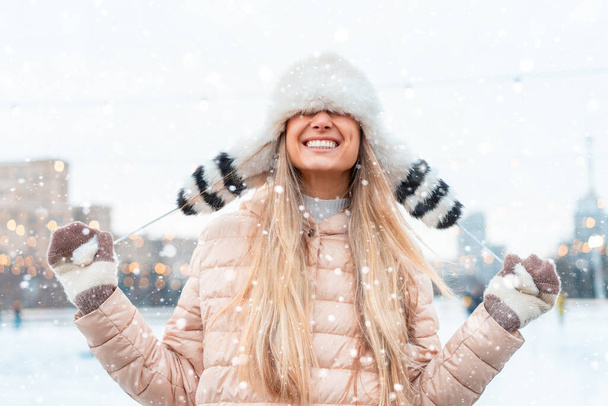 Happy winter time in big city charming girl standing street dressed funny fluffy hat. Enjoying snowfall, expressing positivity, smiling to camera, joyful cheerful mood, true emotions, Christmas mood - Photo, Image