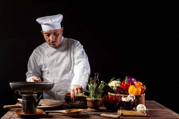 Αρσενικό σεφ σε λευκή στολή δοκιμάζει το φαγητό χρησιμοποιώντας μια ξύλινη κουτάλα στην κουζίνα ενός εστιατορίου πριν από την εξυπηρέτηση, ενώ εργάζονται σε μια κουζίνα εστιατόριο - Φωτογραφία, εικόνα