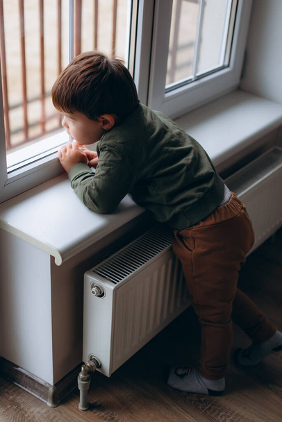 Little, pensive, two years old boy sitting by the window and playing with toy childrens car - Фото, изображение
