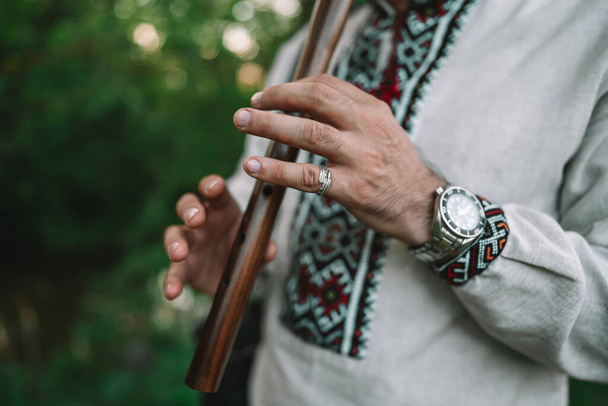 Hands of young man playing on woodwind wooden flute - ukrainian sopilka outdoors. Folk music concept. Musical instrument. Musician in traditional embroidered shirt - Vyshyvanka. - Fotografie, Obrázek