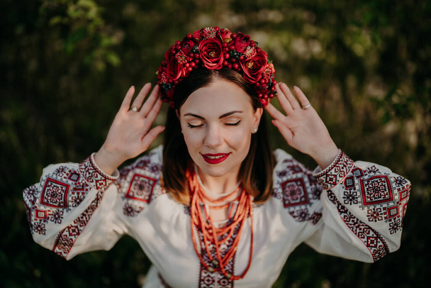 Attractive ukrainian woman in traditional embroidery vyshyvanka dress, ancient coral beads and red flowers wreath. Ukraine, freedom, culture, national costume, victory in war. - Foto, Imagen