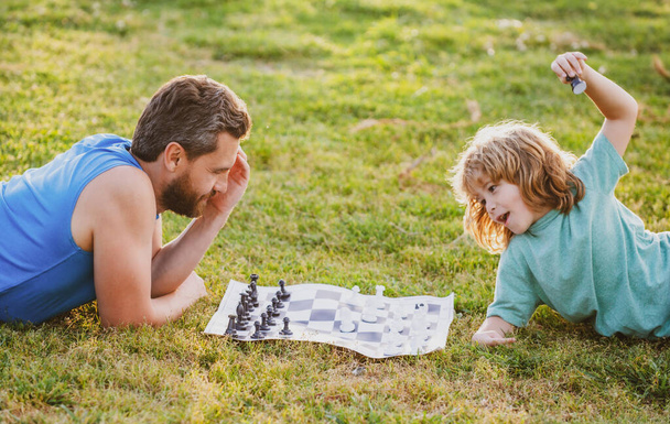 Father and son playing chess lying on grass at lawn park. Fathers Day, love family, parenthood, childhood concept. - Fotografie, Obrázek