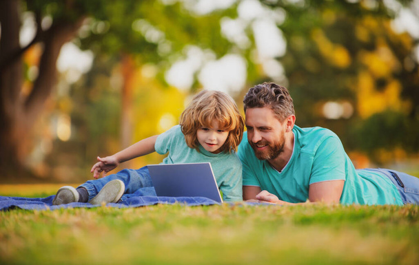 Father and son with a laptop on nature in park. - Zdjęcie, obraz