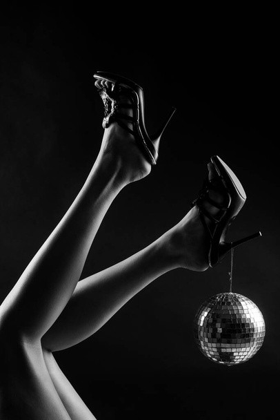 Disco party event. Woman legs with gold disco ball. Celebrate concept. Gold disco ball on high heels. Party concept. - Фото, изображение