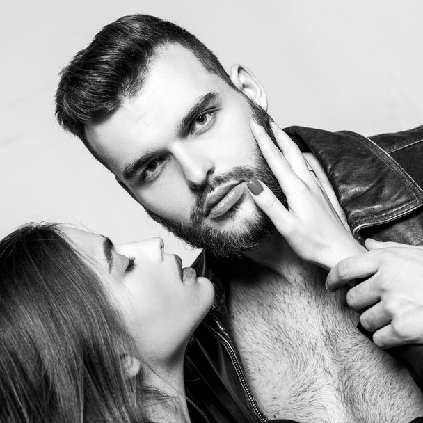 Touch his bristle. She adores male beard. Passionate hug. Passionate couple in love. Man brutal well groomed macho and attractive girl cuddling. Girlfriend passionate red lips and man leather jacket - Photo, image