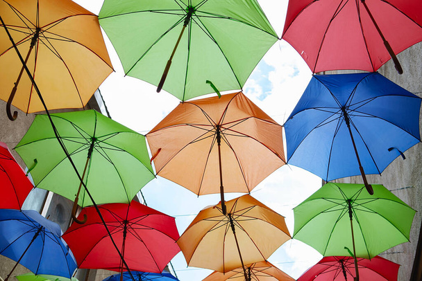 Exposición de paraguas, calle decorada. el cielo está lleno de coloridos paraguas. Muchos paraguas coloridos contra el cielo en los entornos de la ciudad. Fondo de color - Foto, imagen