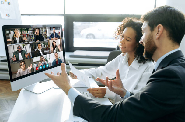 Koledzy biznesowi, współzałożyciele firmy, siedzą przy stole w nowoczesnym biurze przed ekranem komputera, organizują internetową konferencję wideo z międzynarodowymi kolegami, burzę mózgów - Zdjęcie, obraz