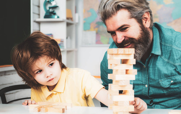 Educational games. Smiling father and focused son playing jenga game at home. - Фото, изображение