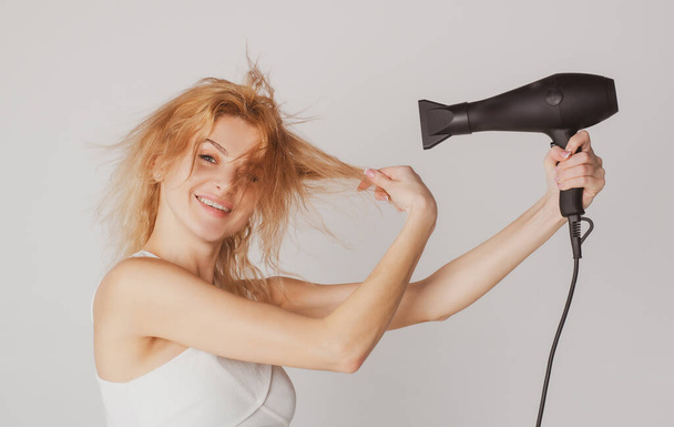 Beautiful caucasian woman posing with wet hair. Women hair treatment. Girl with blonde hair using hairdryer. Hairstyle, hairdressing concept. - Valokuva, kuva