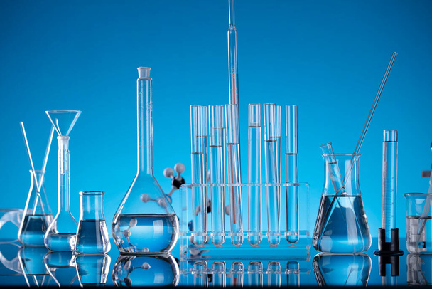 Laboruntersuchungen in Bezug auf Tests und Medikamente gegen Covid. Mikroskop, Shethoskop, Glasröhren und Becher auf blauem Hintergrund. - Foto, Bild