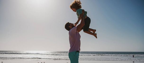 Father throws son up against the blue sky. Handsome man father carrying young boy son. Happy dad holding child. Dad throwing child. Happy family concept. - Foto, Imagen