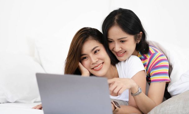 A couple of lovely woman listening song and watch movie with laptop   in bed while smiling. They are happiness and building good relationships in the future - Photo, Image