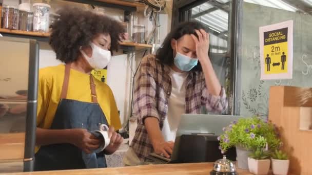 Zwei junge Café-Barista-Partner und Unternehmer in Schürzen arbeiten mit Gesichtsmasken in einem Coffeeshop, betreuen Start-up-Jobs in einem neuen normalen Lebensstil, Auswirkungen der COVID19-Pandemie auf das KMU-Geschäft. - Filmmaterial, Video