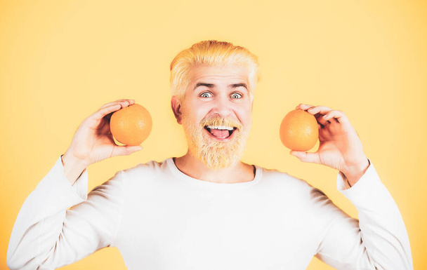 Smiling funny man with oranges in hands. Handsome young man hold fresh natural orange. Man enjoying fruit refreshment orange on orange backgroung isolated. - Photo, Image