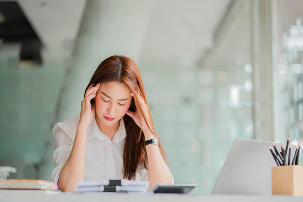 Asiatische Geschäftsfrau, die eine Firma besitzt Sie hatte Kopfschmerzen, als sie lange auf ihren Laptop-Bildschirm und ihre Dokumente starrte. macht sie müde und schwindelig Augenbelastung Konzept der Berufskrankheit - Foto, Bild