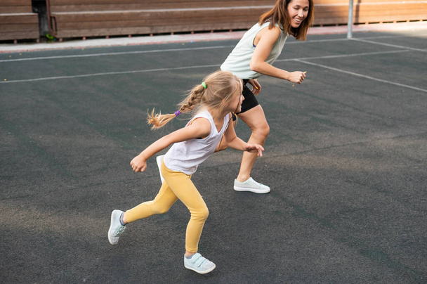Mujer caucásica entra a hacer deporte con su hija al aire libre. Una colegiala y su madre están corriendo por el estadio. - Foto, imagen
