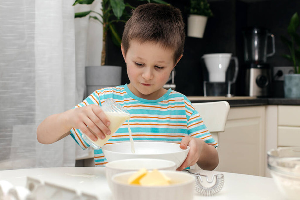 Il ragazzo prepara la pasta per il biscotto o la cottura in cucina. Il bambino aggiunge latte alla ciotola. Piccolo chef e aiutante in cucina. - Foto, immagini