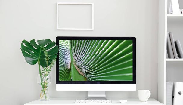 Munkahely modern számítógéppel és trópusi levéllel vázában a fényfal közelében - Fotó, kép
