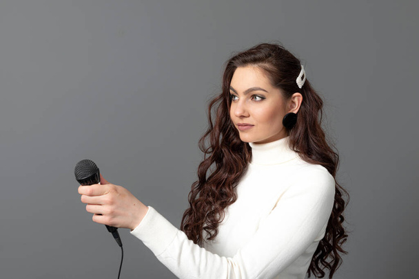 young female journalist is standing and stretching a microphone forward, isolated on gray - Fotoğraf, Görsel