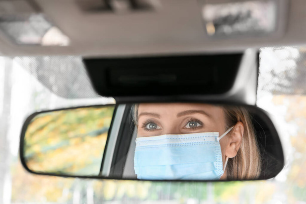 Reflection of female driver wearing medical mask in car rear view mirror - Fotografie, Obrázek