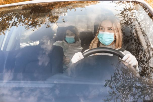 女性ドライバーと車の中で医療マスクを身に着けている乗客 - 写真・画像