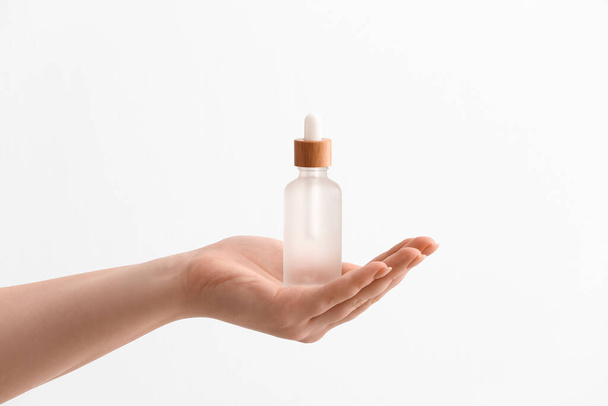 Female hand with bottle of serum on white background, closeup - Photo, Image