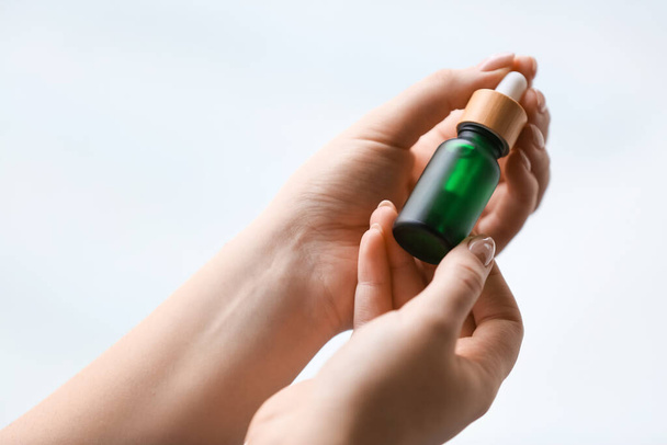 Female hands with bottle of serum on light background, closeup - Zdjęcie, obraz