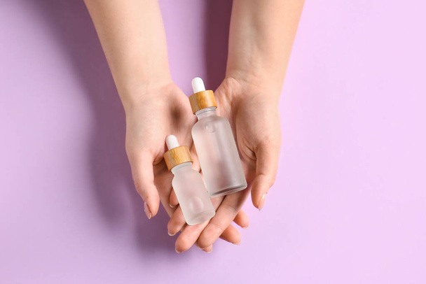 Female hands with bottles of serum on lilac background, closeup - Foto, Imagen