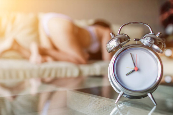 Pehmeä valo ja hämärtynyt kuva herätyskello sijoitettu sängyn viereen heräsi määräaikaan mennessä naisen herätä ja valmistautua lähtemään töihin ajoissa. Ajatus hälytyksen asettamisesta herätyskellolla - Valokuva, kuva