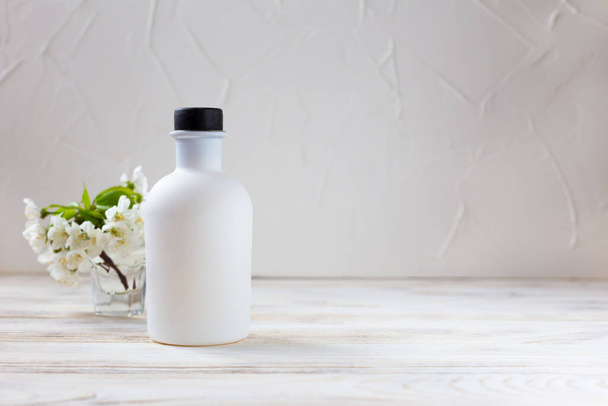 Λευκό μπουκάλι και λουλούδια σε ελαφρύ φόντο - Φωτογραφία, εικόνα