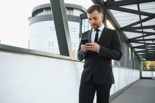 Portrait of an excited young businessman dressed in suit holding mobile phone, celebrating - Photo, image
