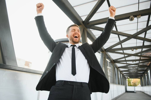 Successful businessman celebrating his victory with arms up on cityscape background - Photo, image