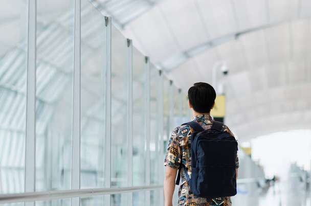 Азиатский мужчина с сумкой стоит и с нетерпением ждет, чтобы путешествовать после пандемии. Путешествия и отдых. - Фото, изображение