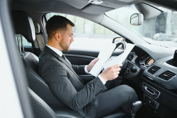 Always in a hurry. Handsome young man in full suit smiling while driving a car - Zdjęcie, obraz