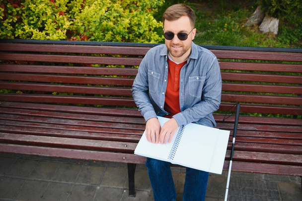 Blind man reading book on bench in park. - Photo, Image