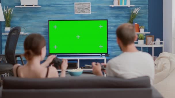 Powrót widok młodej kobiety i chłopaka graczy gospodarstwa kontrolerów gry akcji na konsoli na zielony ekran telewizora - Materiał filmowy, wideo