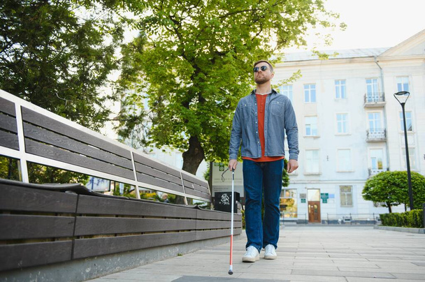young blind man with white cane walking across the street in city. - Foto, afbeelding