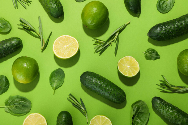 Flat lay with cucumbers, limes, basil and rosemary on green background - Photo, Image